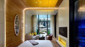 A modern hotel room with a wooden ceiling, a large bed, a seating area with a sofa and chairs, a TV, and a view of a waterfall outside.