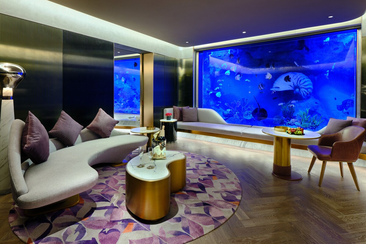 A modern lounge area with a large aquarium, comfortable seating, and a decorative rug.