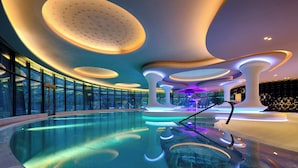 Een modern binnenzwembad met een glazen afscheiding, omringd door vloeiende architectonische vormen en sfeerverlichting.