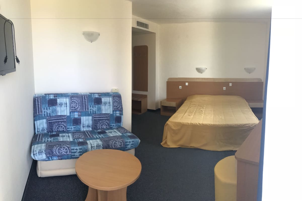 A hotel room with a sofa, a bed, a small table, and a wall-mounted lamp.