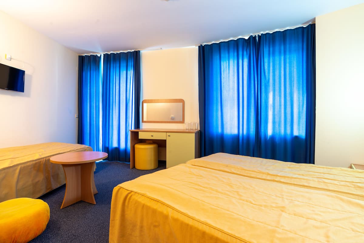 A hotel room with a bed, a desk with a chair, a small round table, and a television on the wall.