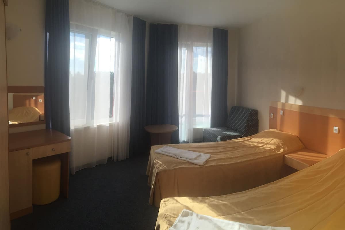 A hotel room with two single beds, a wooden desk, a chair, and a small table.