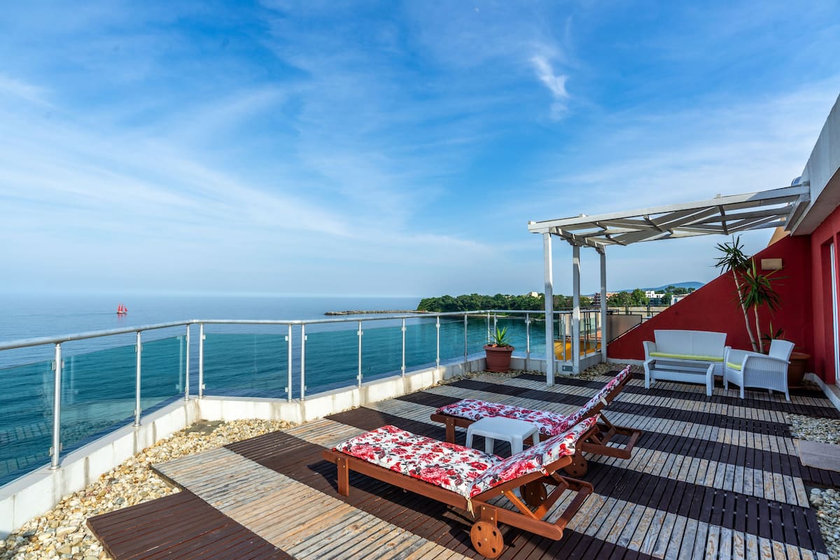 A deck with wooden flooring, lounge chairs, and a table with a red and white patterned tablecloth.