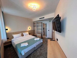 A hotel room with a bed, bedside tables, a TV mounted on the wall, and a walk-in closet. - Family Hotel Sunday (Kiten)