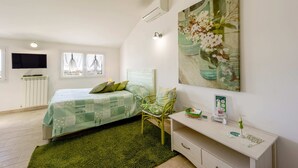 A bedroom with a bed, a chair, a bedside table, a TV, and a painting on the wall. - Agriturismo Le Girandole (Diano Marina)