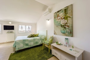 Un dormitorio con cama, una silla, una mesita de noche, un televisor y un cuadro en la pared.