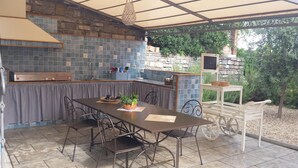 An outdoor kitchen area with a stone wall, a built-in grill, and a table with chairs. - Agriturismo Le Girandole (Diano Marina)