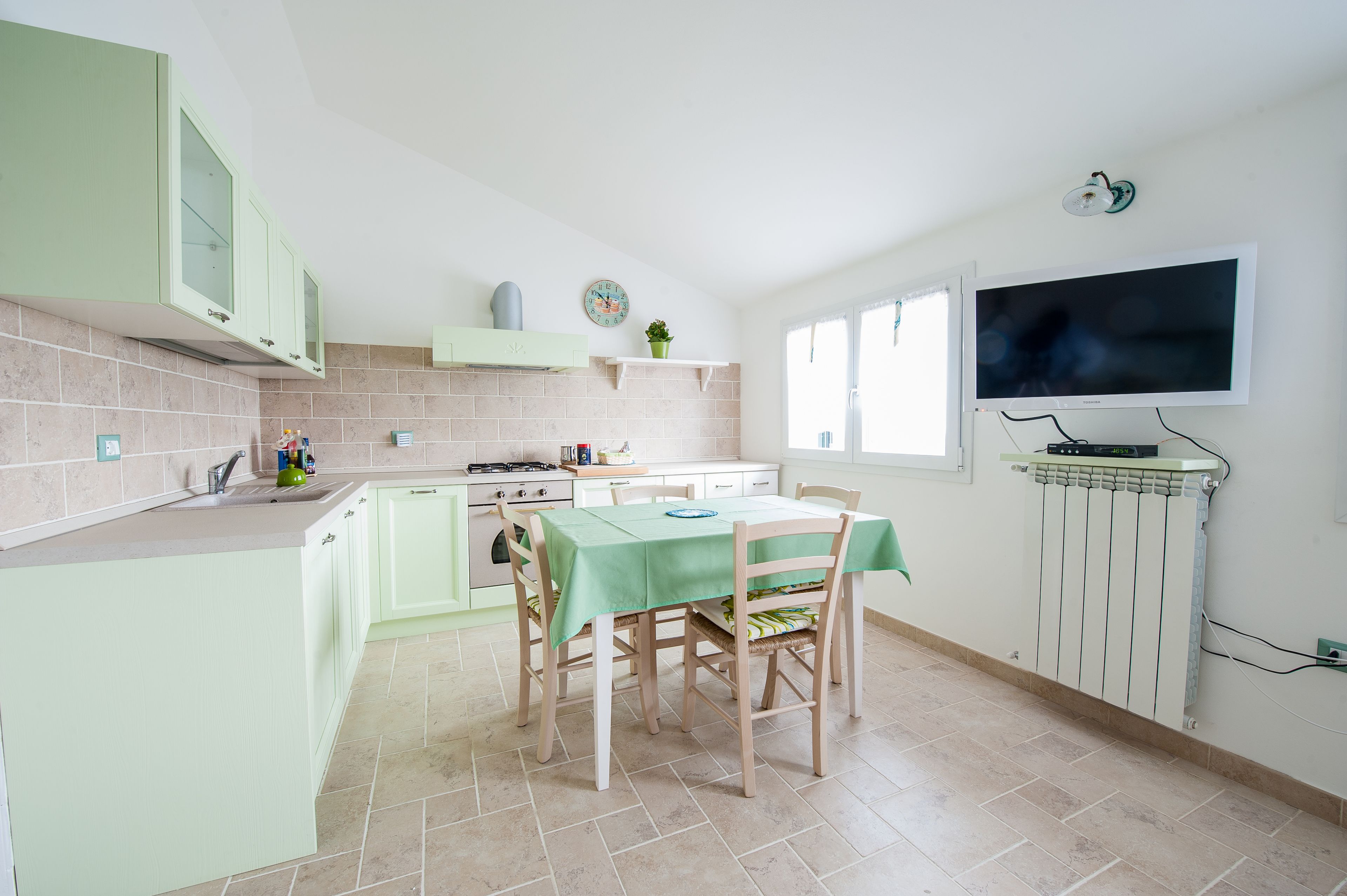 Una cocina con una mesa de comedor, sillas, un televisor y una ventana.