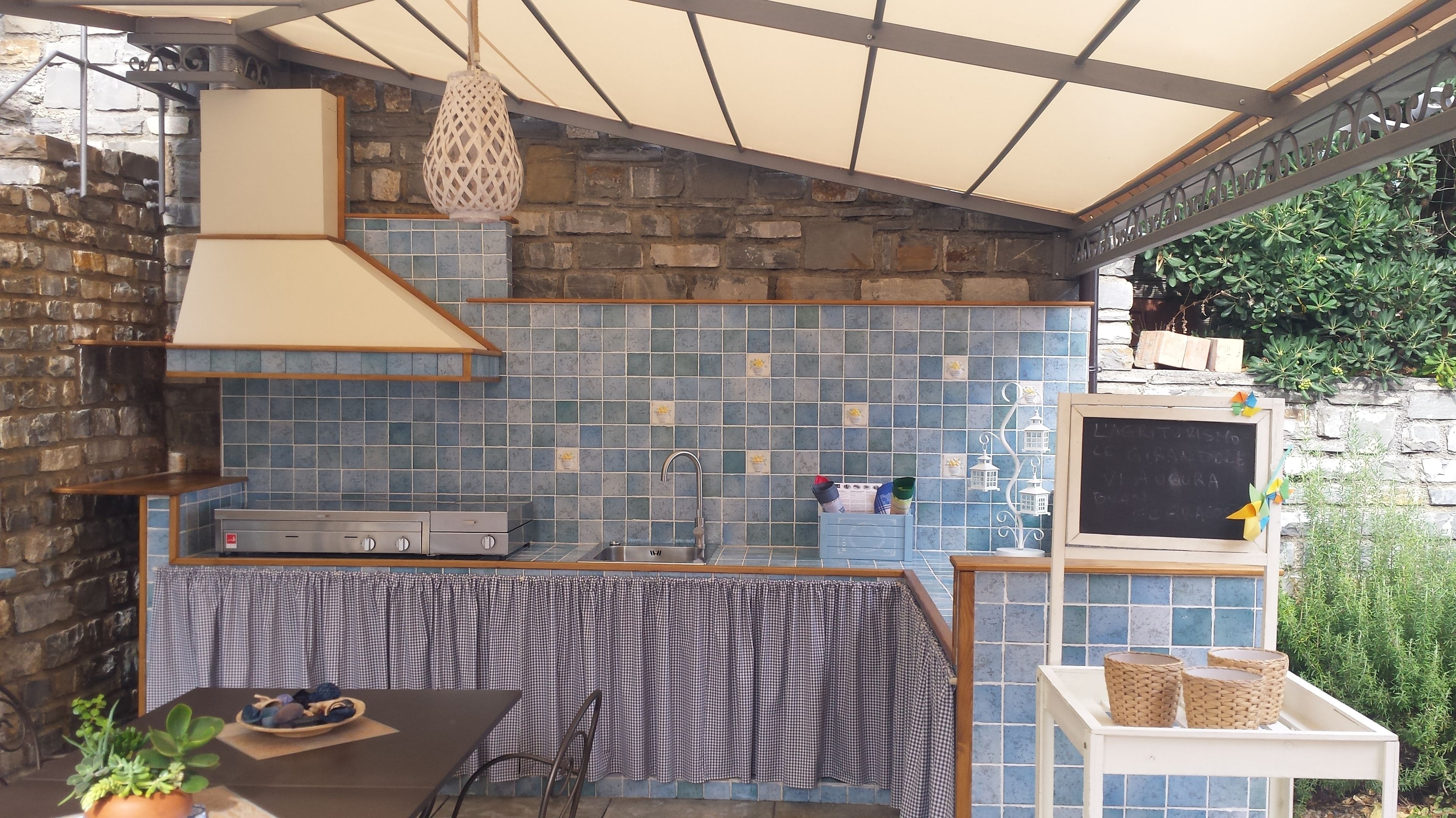 Une cuisine extérieure dotée d’un mur recouvert de carreaux, d’une cuisinière à gaz et d’un luminaire suspendu.