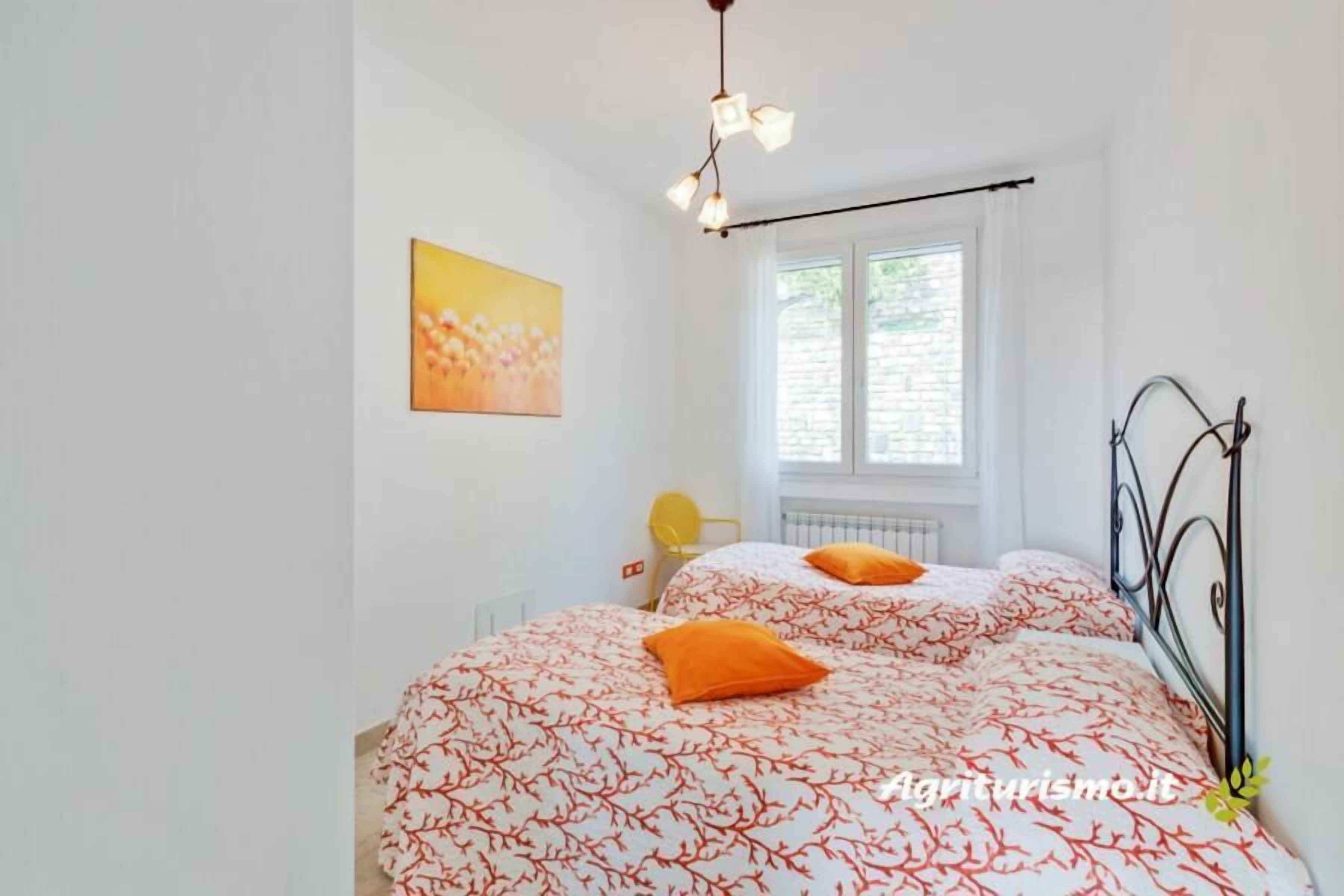 Un dormitorio con dos camas, una ventana, un radiador y un cuadro en la pared.
