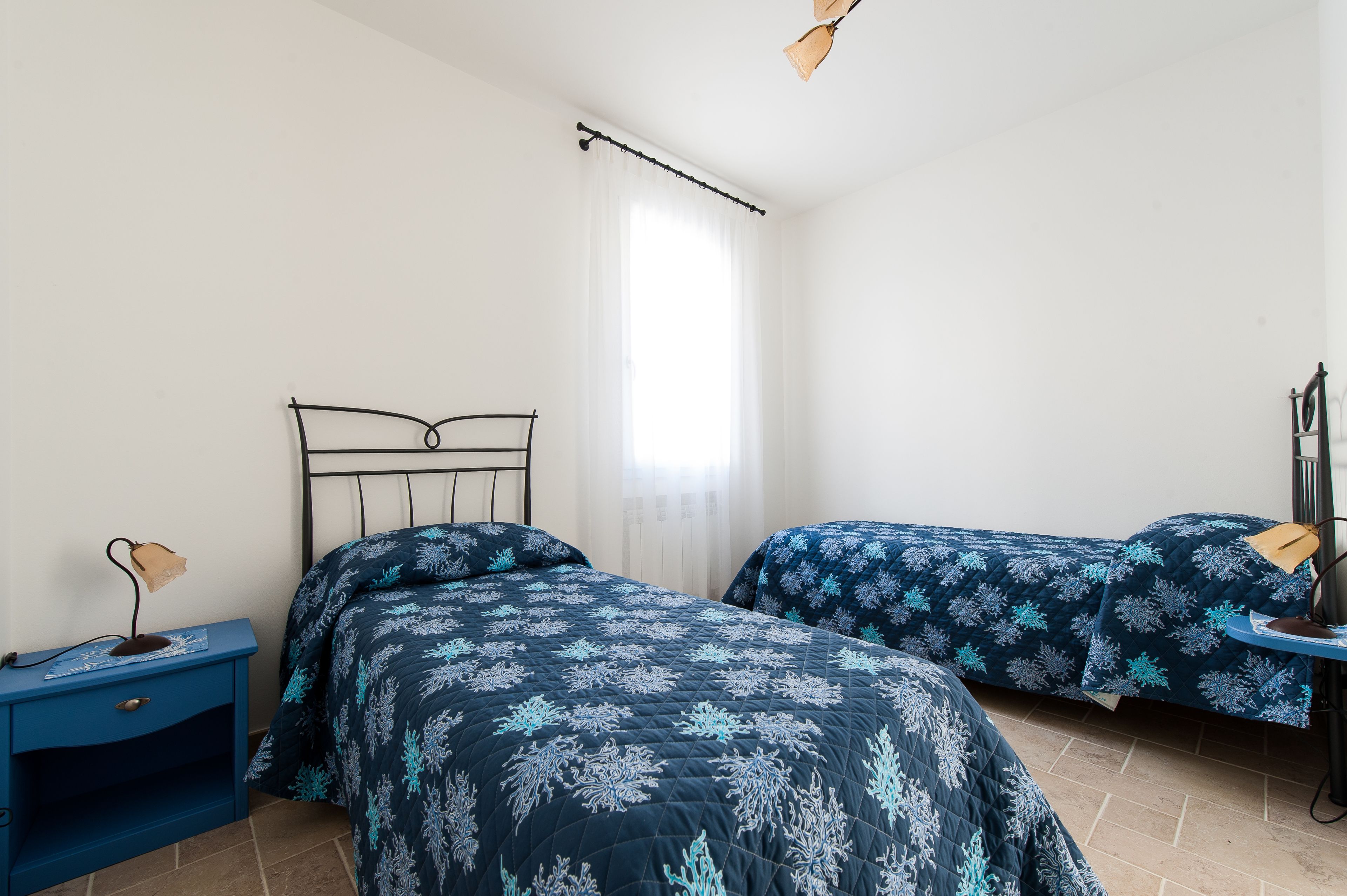 Une chambre avec deux lits, une table de chevet, une lampe et une fenêtre avec des rideaux.