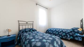 Une chambre avec deux lits, une table de chevet, une lampe et une fenêtre avec des rideaux.