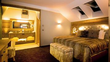 Une chambre à coucher avec un grand lit, un banc, une commode et une salle de bain équipée d’un miroir et d’un lavabo.