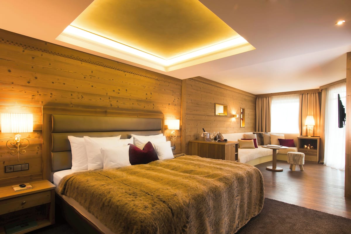 A hotel room with a large bed, a small table, a sofa, and a nightstand with a lamp.