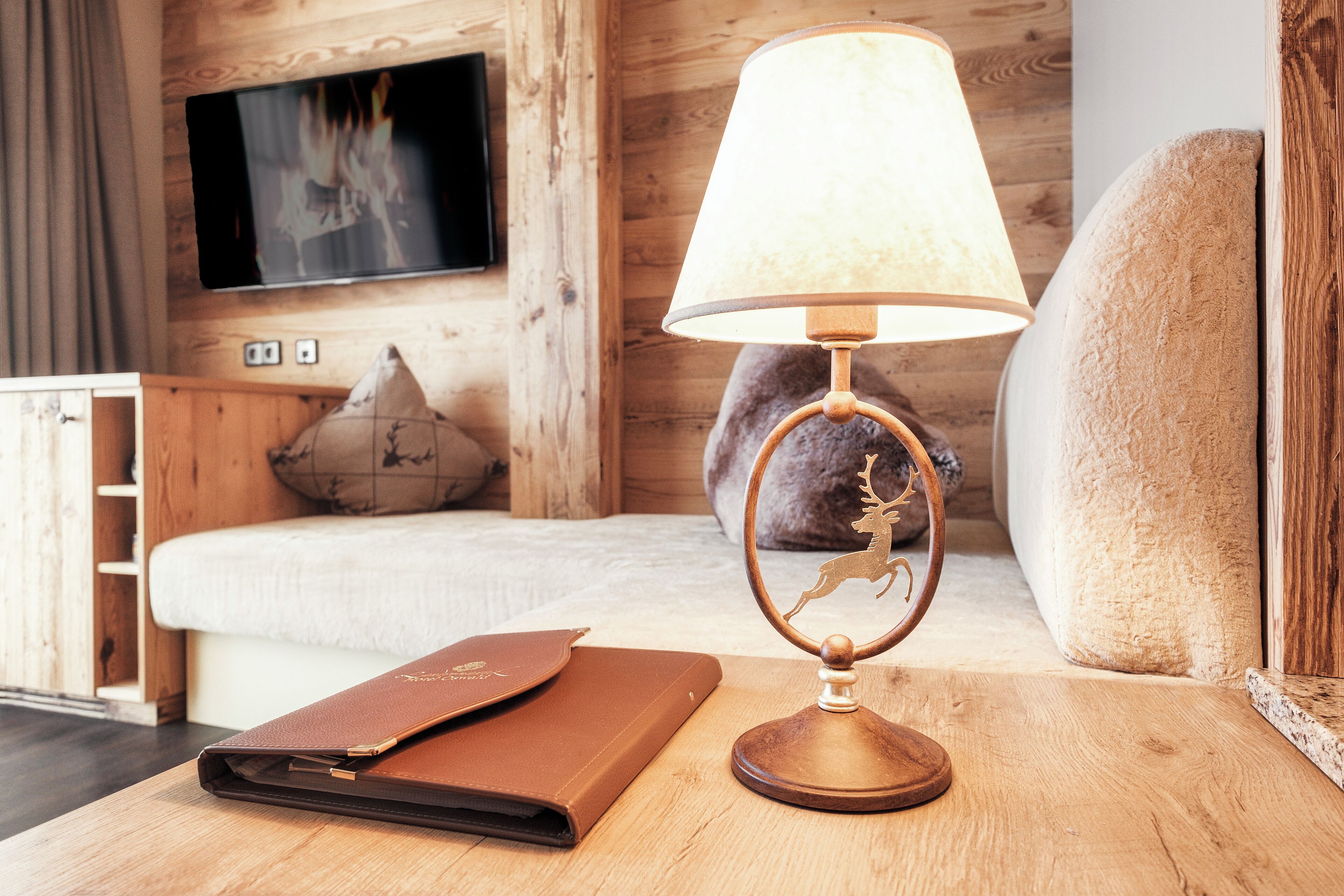 A wooden table with a lamp, a leather-bound book, a plush sofa, and a television mounted on the wall.
