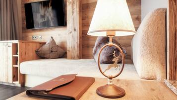 A wooden table with a lamp, a leather-bound book, a plush sofa, and a television mounted on the wall.