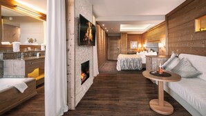 A modern hotel room with a fireplace, a bed, a sitting area with a table, and a large mirror. - Landromantik Hotel Oswald Gourmet & SPA (Teisnach)