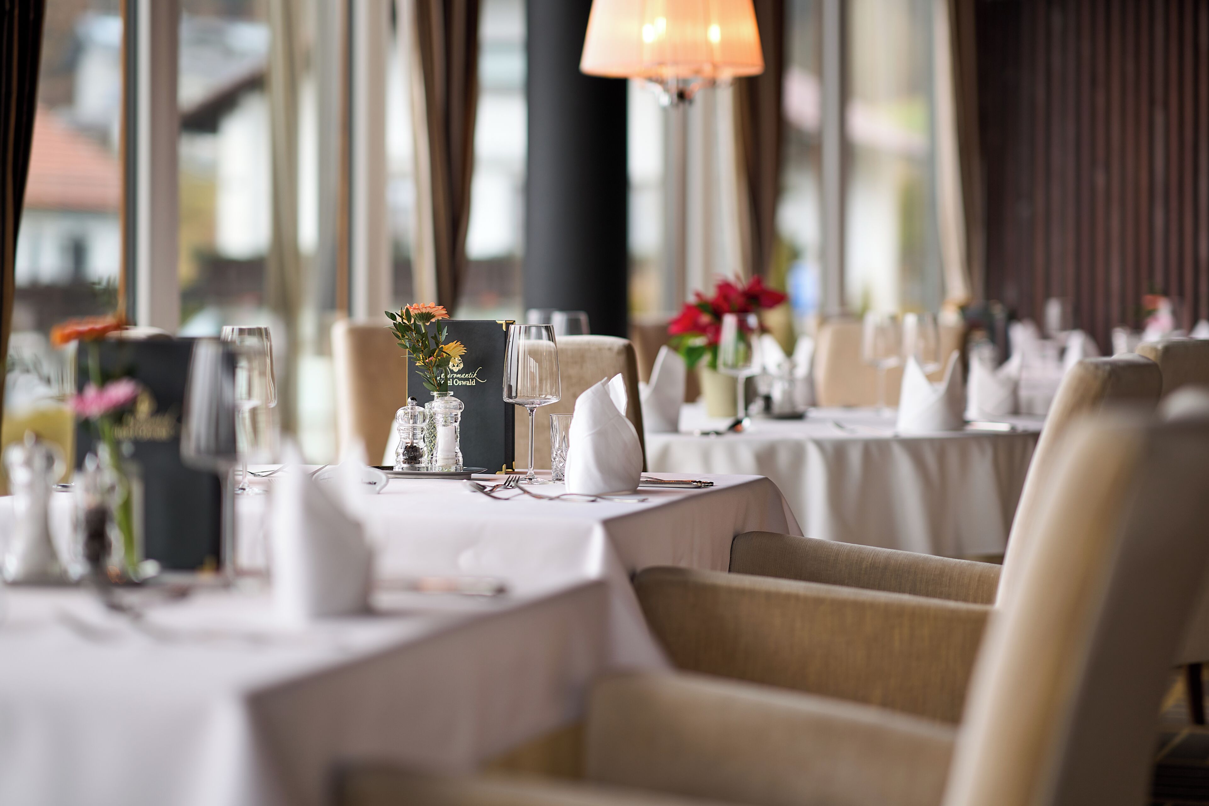Un restaurant où les tables sont dressées pour le service, avec des nappes blanches et une vaisselle soigneusement disposée.
