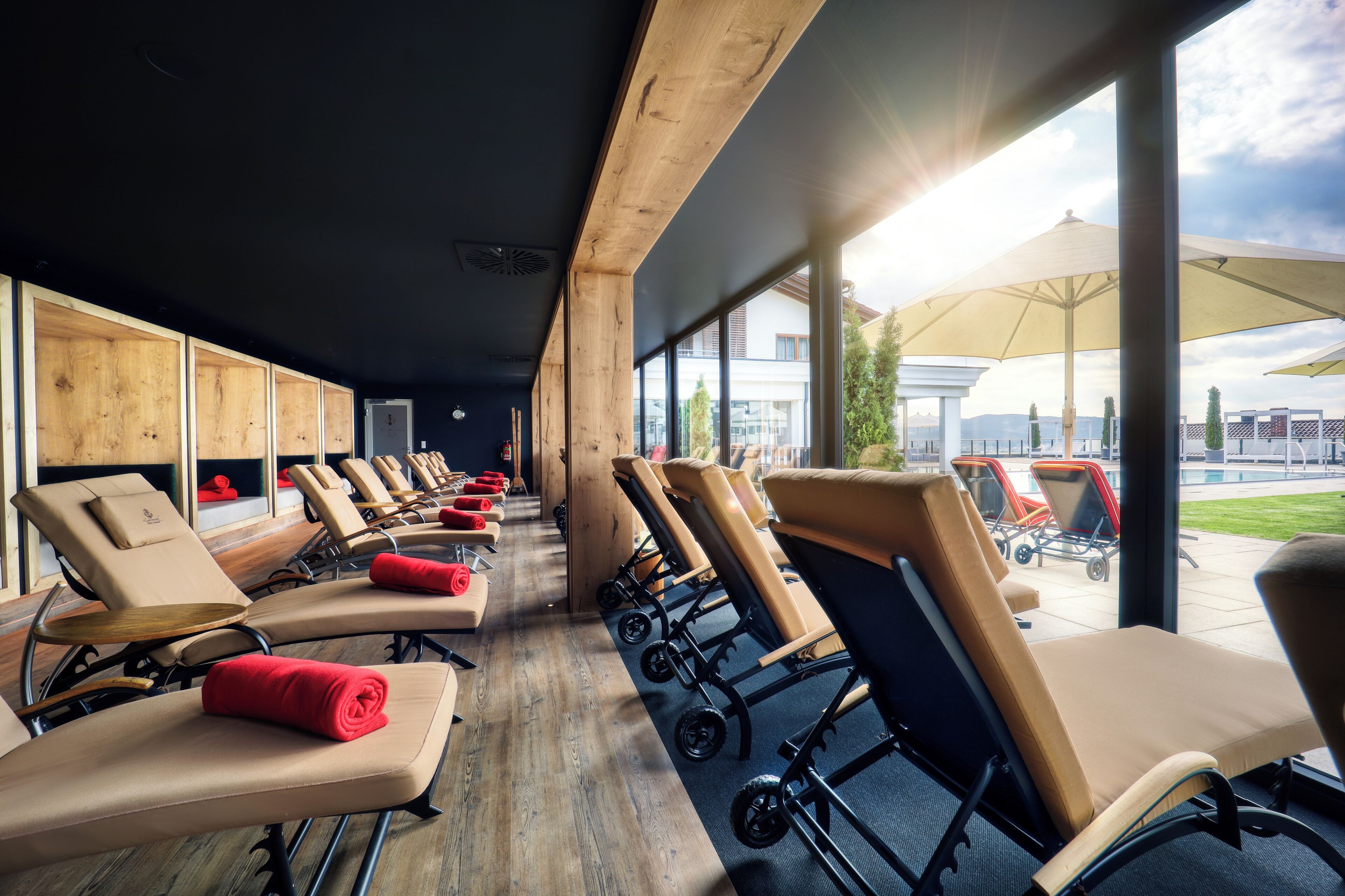 A row of sun loungers with towels, wooden cabinets, and large windows with a view of the outdoors.