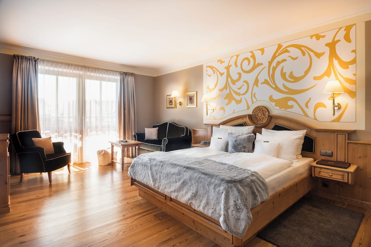A hotel room with a large bed, a sitting area with a chair and a small table, and a large window with curtains.