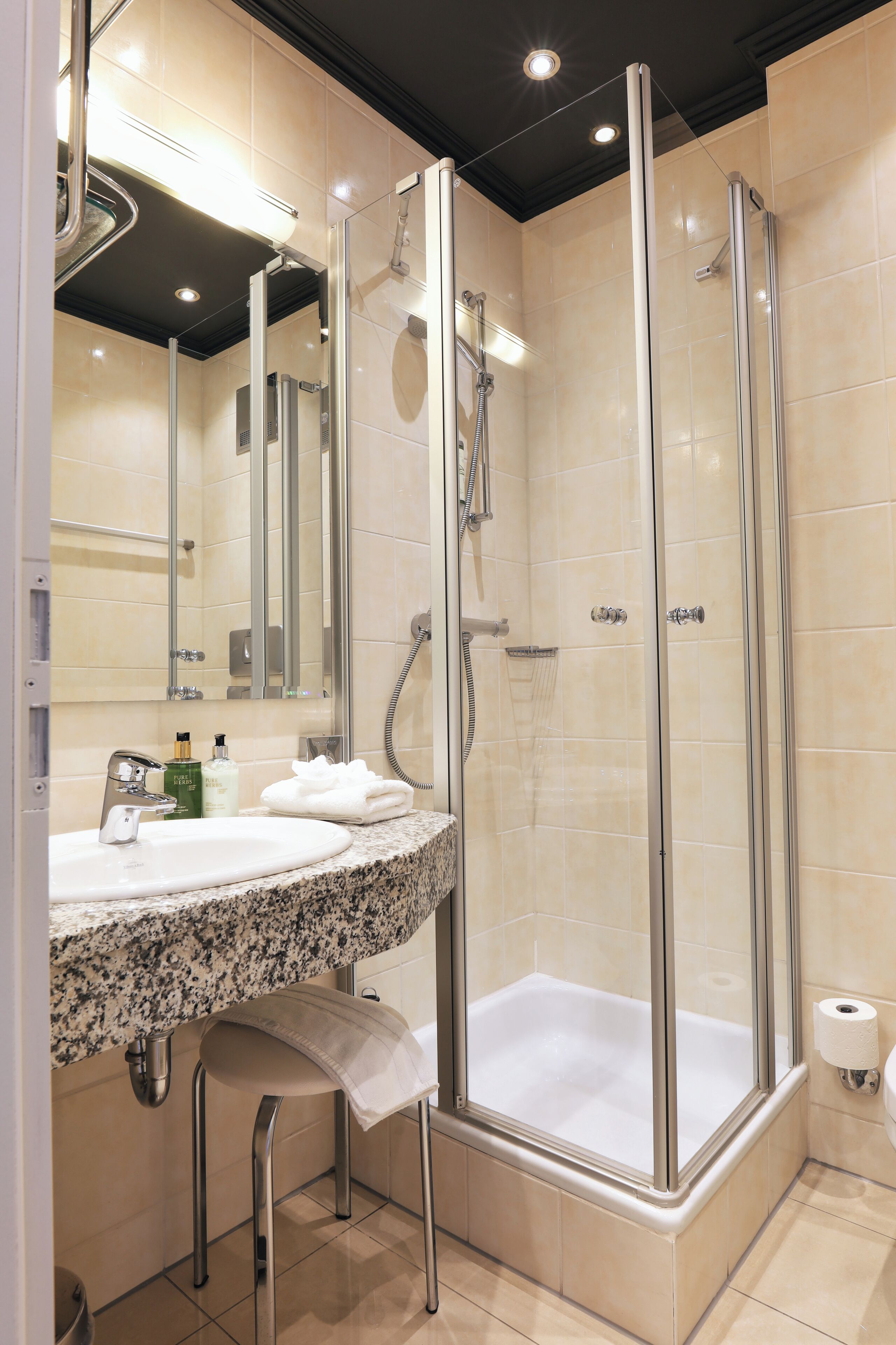 Un baño moderno con ducha de vidrio, lavamanos de granito y un espejo sobre el lavamanos.