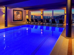An indoor swimming pool with a sunset view, lounge chairs, and a decorative wall. - Landromantik Hotel Oswald Gourmet & SPA (Teisnach)