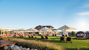 A resort with outdoor seating and umbrellas, a pool, and a building with a balcony. - Landromantik Hotel Oswald Gourmet & SPA (Teisnach)
