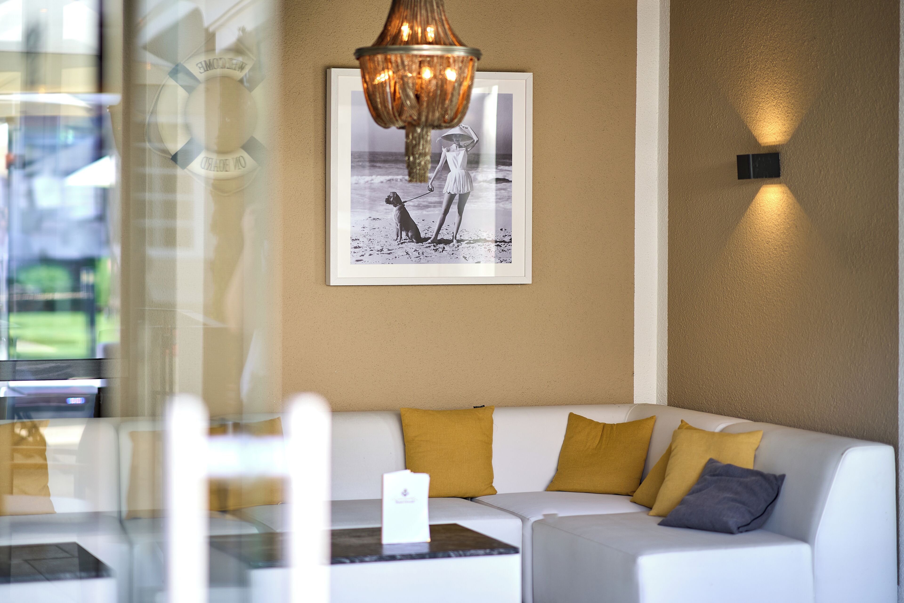 A modern interior with a white sofa, mustard and gray pillows, a framed photograph on the wall, and a hanging light fixture.