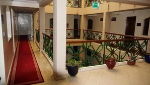 Un couloir d’hôtel avec un tapis rouge, des rampes vertes et des plantes en pot.