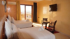 Une chambre d’hôtel avec deux lits, une télévision, une petite table avec des chaises et une vue sur la mer, visible à travers la porte-fenêtre coulissante.