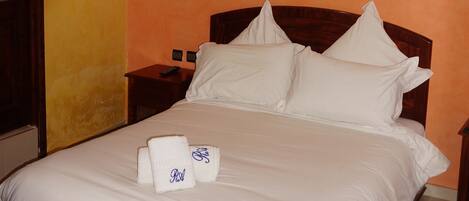 A neatly made bed with white linens and pillows, a wooden headboard, and a bedside table with a remote control.