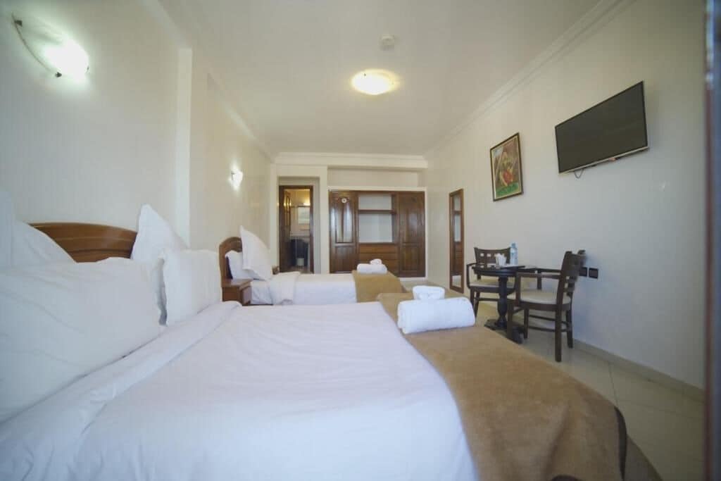 A hotel room with two beds, a desk, and a television.