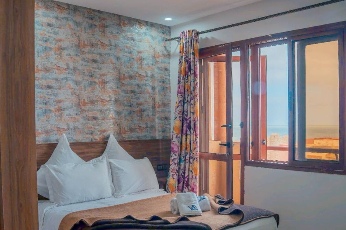 A hotel room with a bed, a window with curtains, a wooden headboard, and a tiled floor.