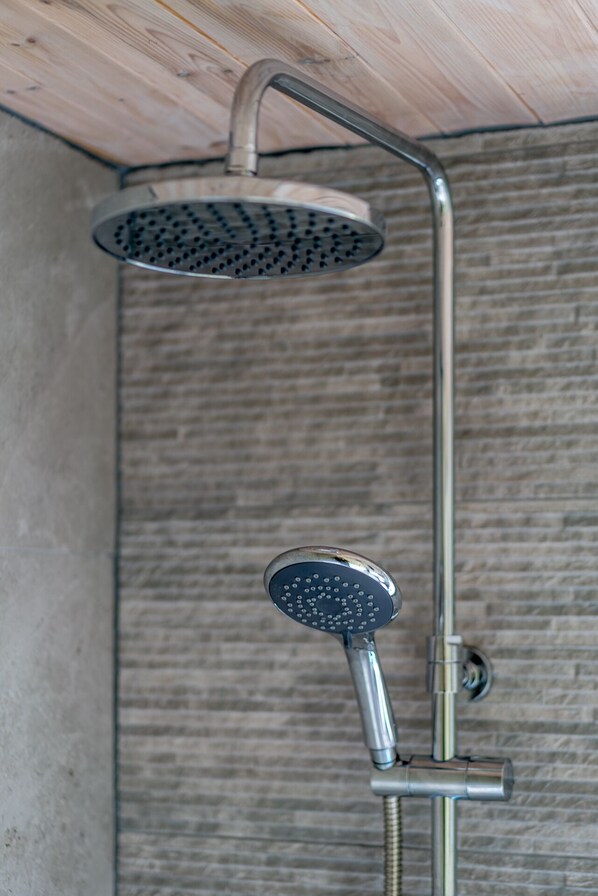 A shower with a rain showerhead and handheld showerhead mounted on a wall with a textured surface.