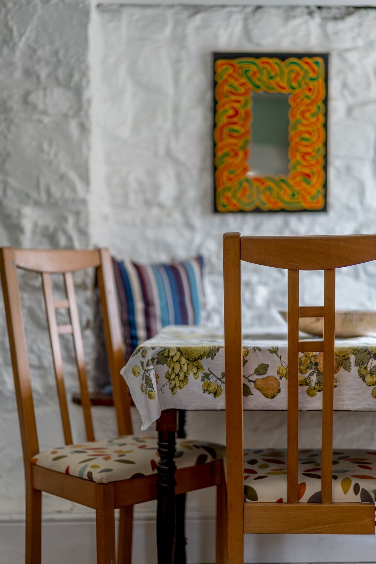 Un comedor con una silla y una mesa de madera, un cojín a rayas y una obra de arte colorida enmarcada en la pared.