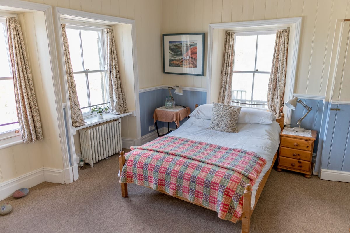 A bedroom with a bed, a nightstand, a radiator, and a window with curtains.