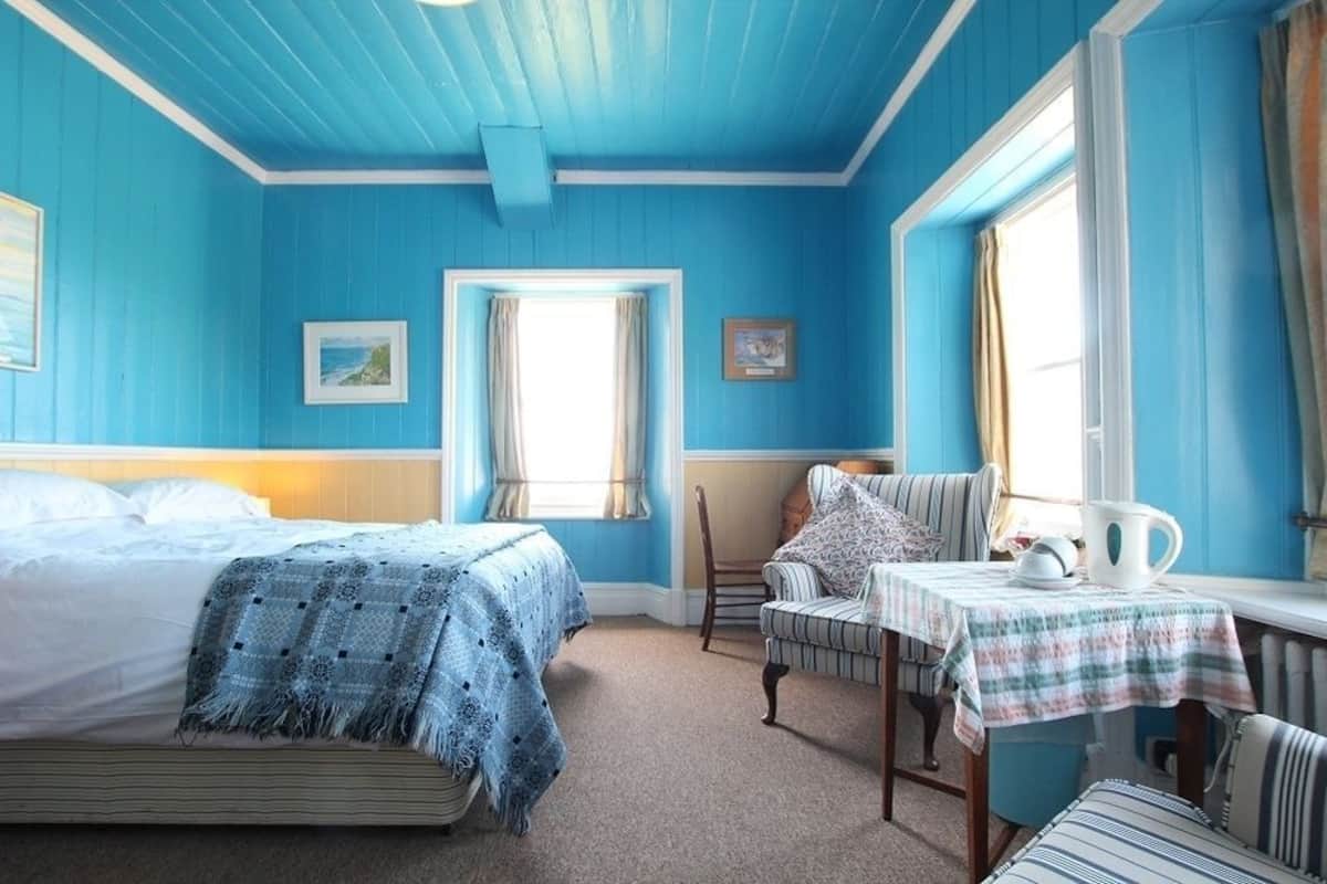 A room with a bed, a chair, a small table with a pitcher, and a window with curtains.