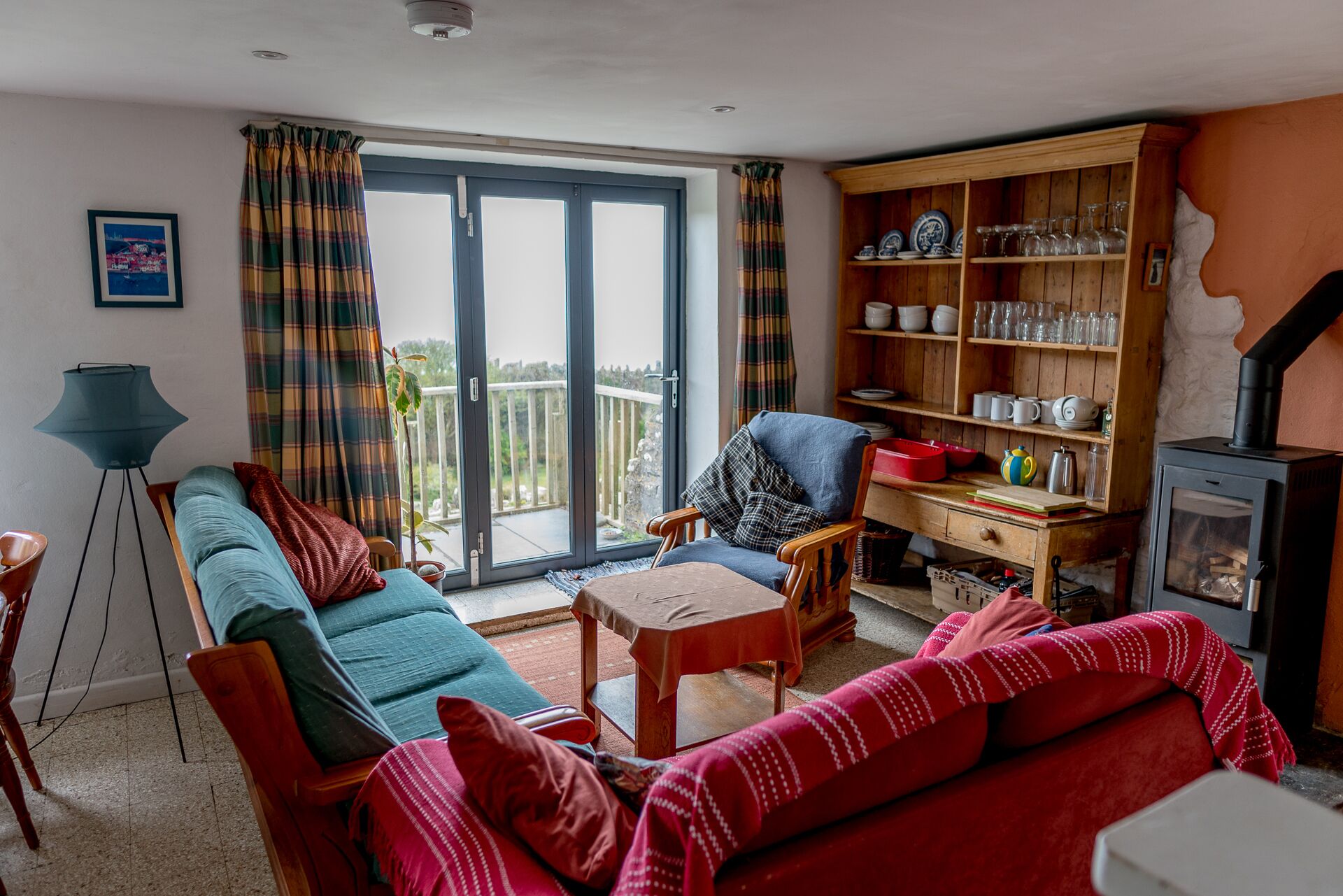 A cozy living room with a sofa, armchair, and a wooden bookshelf filled with dishes and glasses.