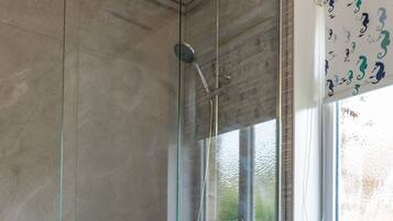 A bathroom with a glass-enclosed shower, a blue chair with towels, and a window with seahorse curtains.