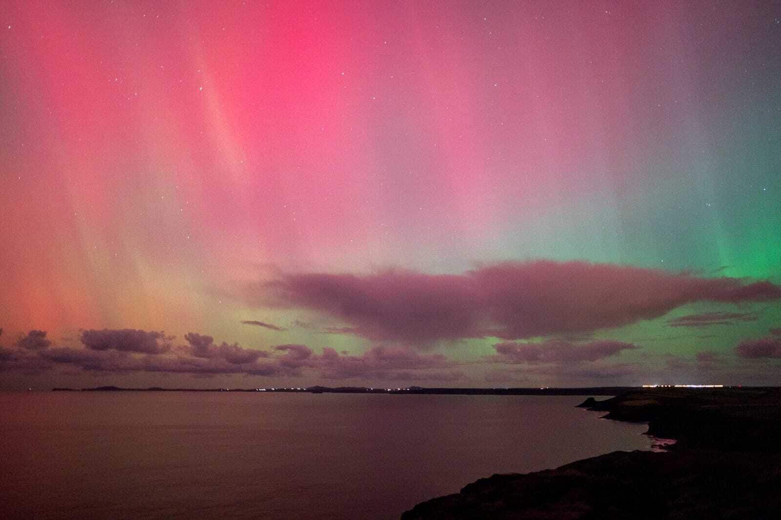 Céu noturno com a aurora boreal sobre águas calmas.