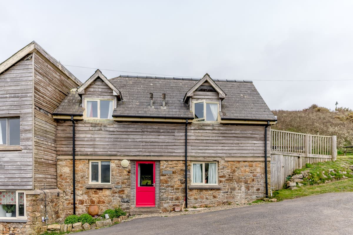 A two-story stone house with a red door, a stone exterior, and a wooden fence.