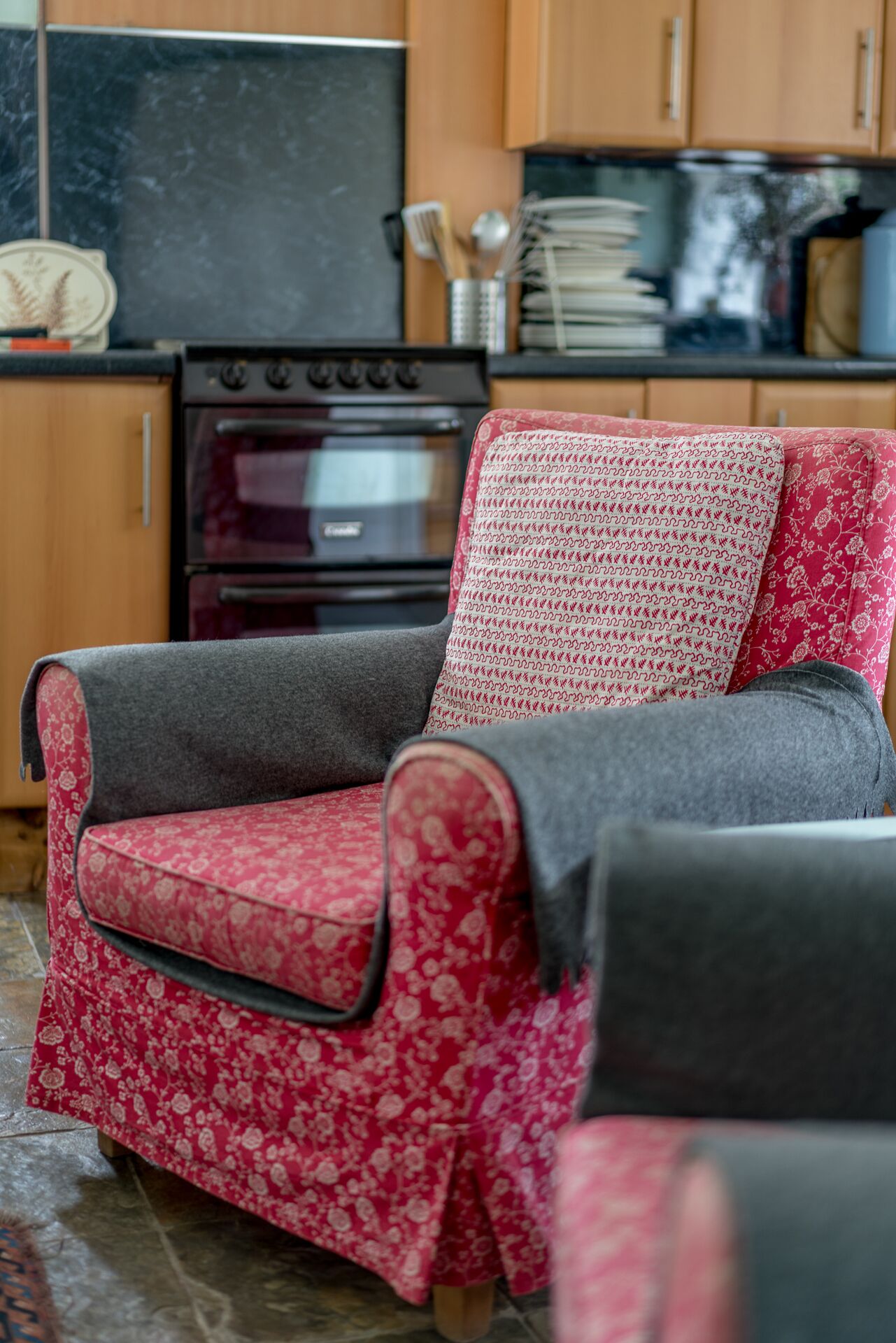 A red floral sofa with a grey throw blanket in a kitchen area.