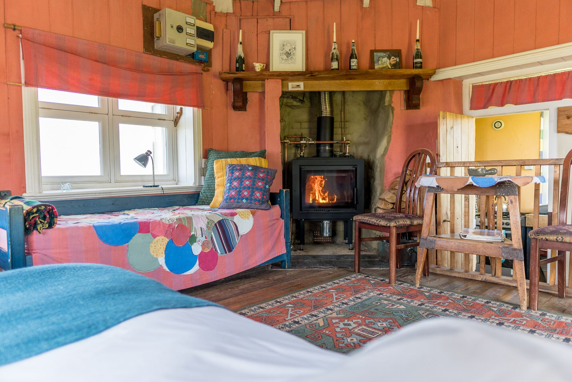 A cozy room with a bed, a wooden chair, a rug, a fireplace, and a shelf with various items.