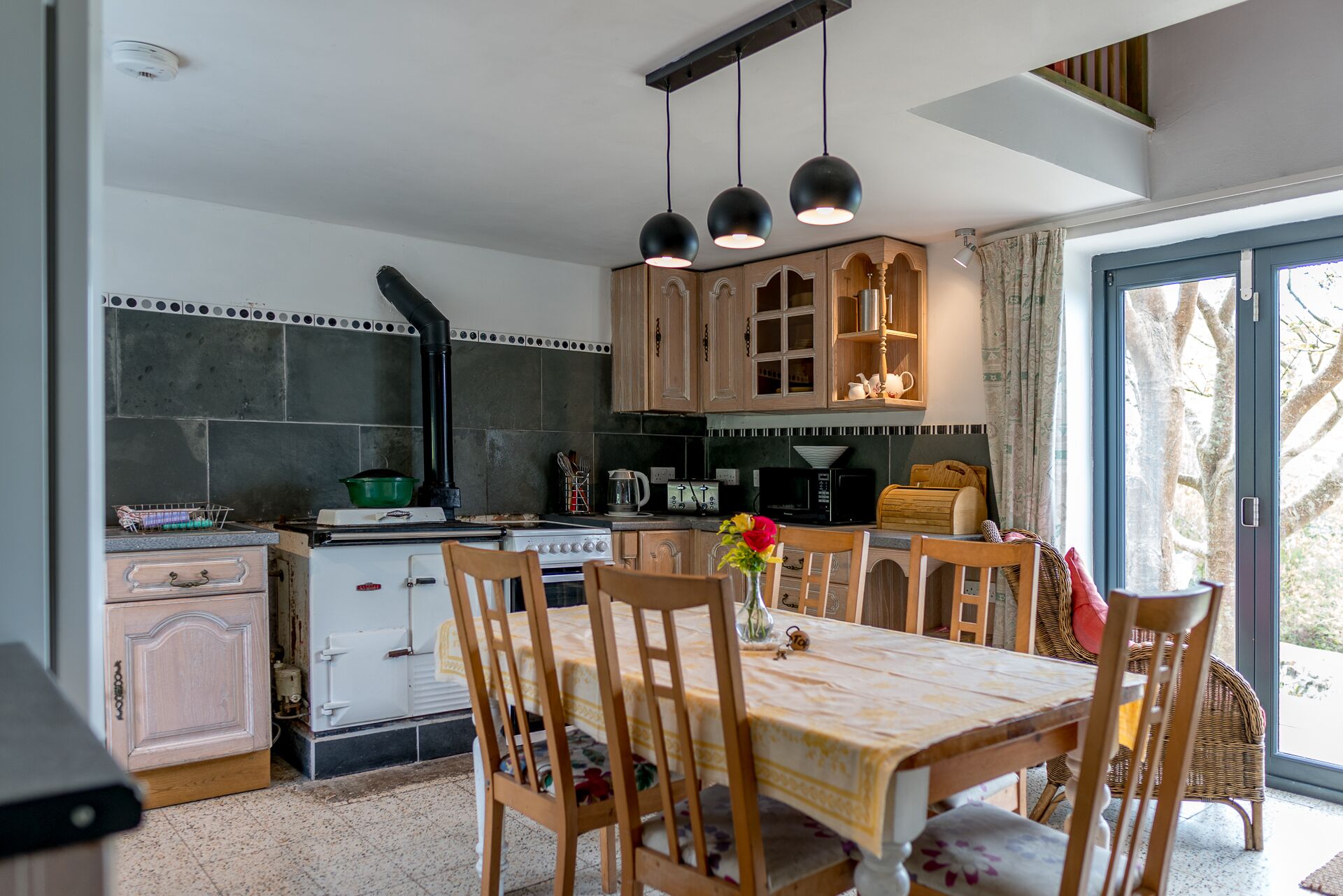 A kitchen with a stove, microwave, and cabinets. There is a dining table with chairs and a vase with flowers.