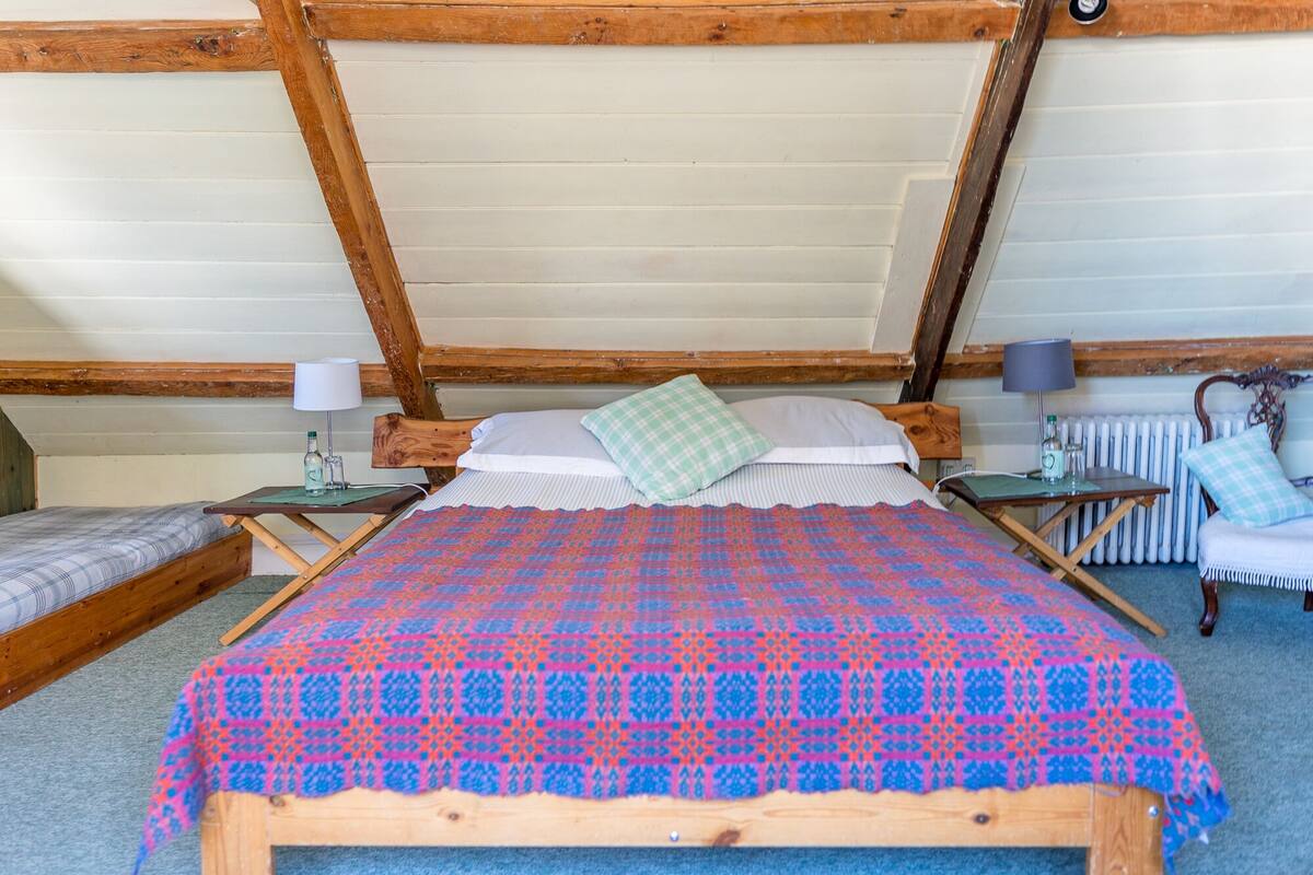 A cozy attic bedroom with a wooden bed, a small table with a lamp, and a radiator.