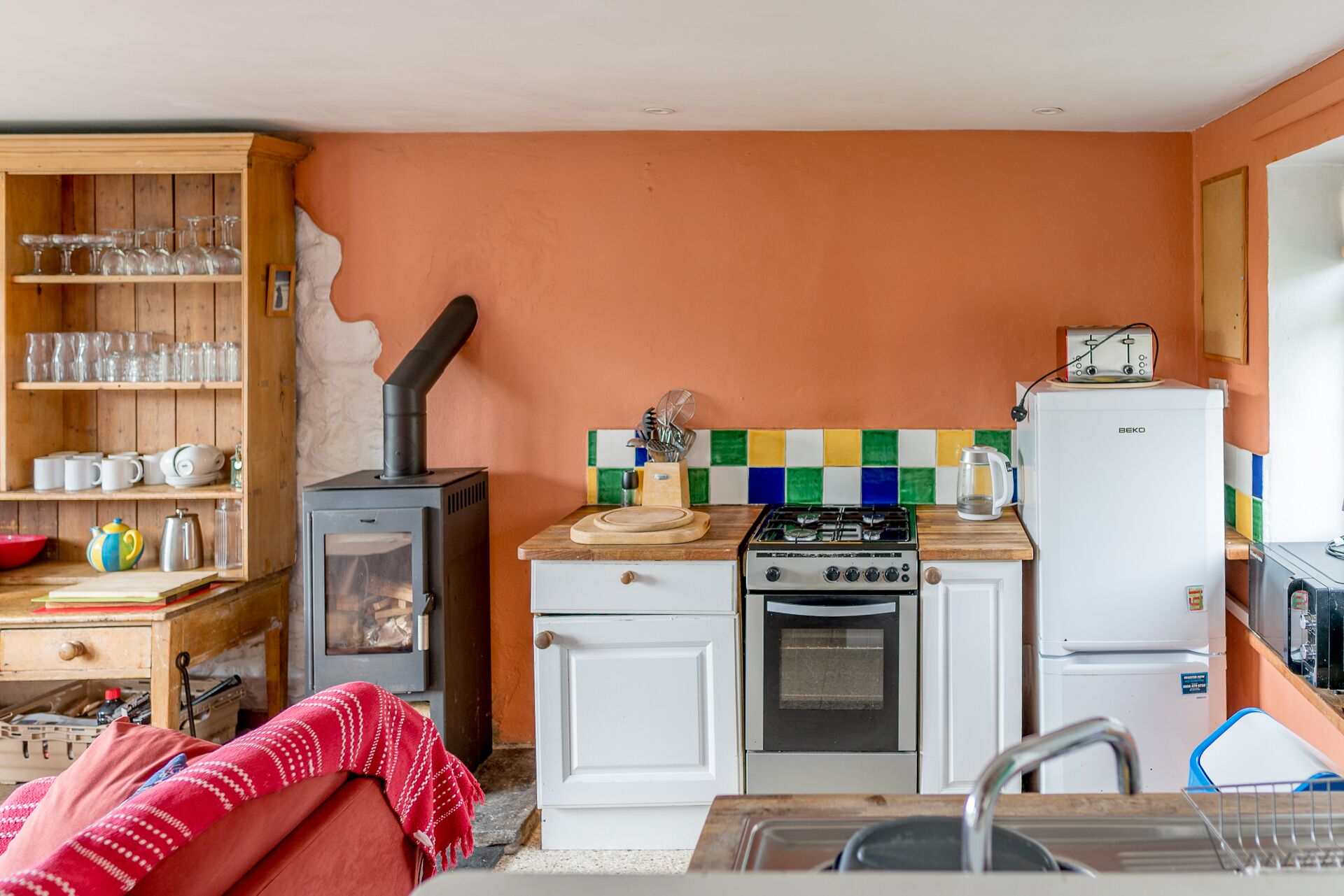 A compact kitchen with a wood stove, a gas stove, an oven, and a refrigerator.