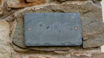 A slate sign with the inscription "BYRE" mounted on a stone wall.