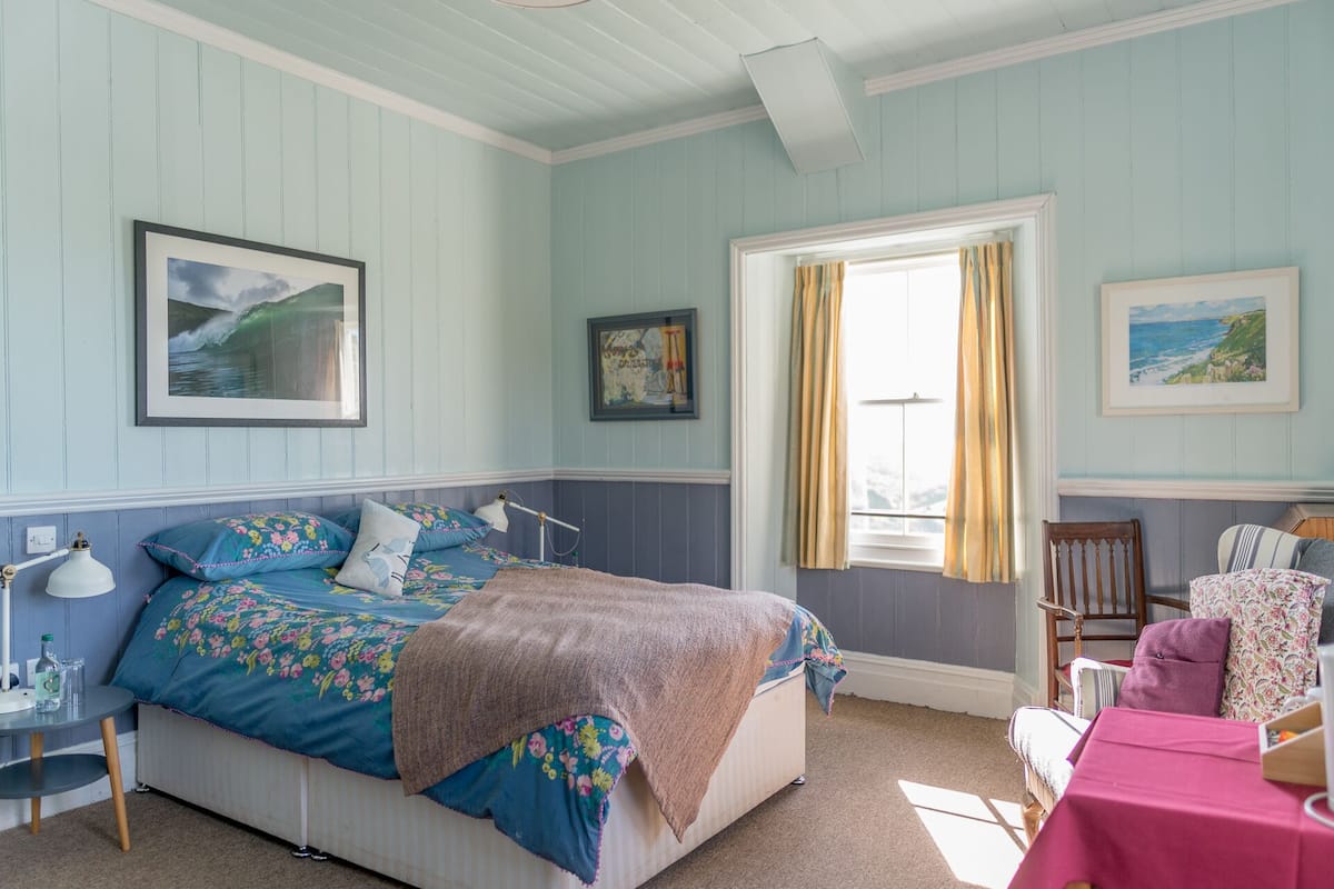 A bedroom with a bed, a desk, a chair, and a window with curtains.