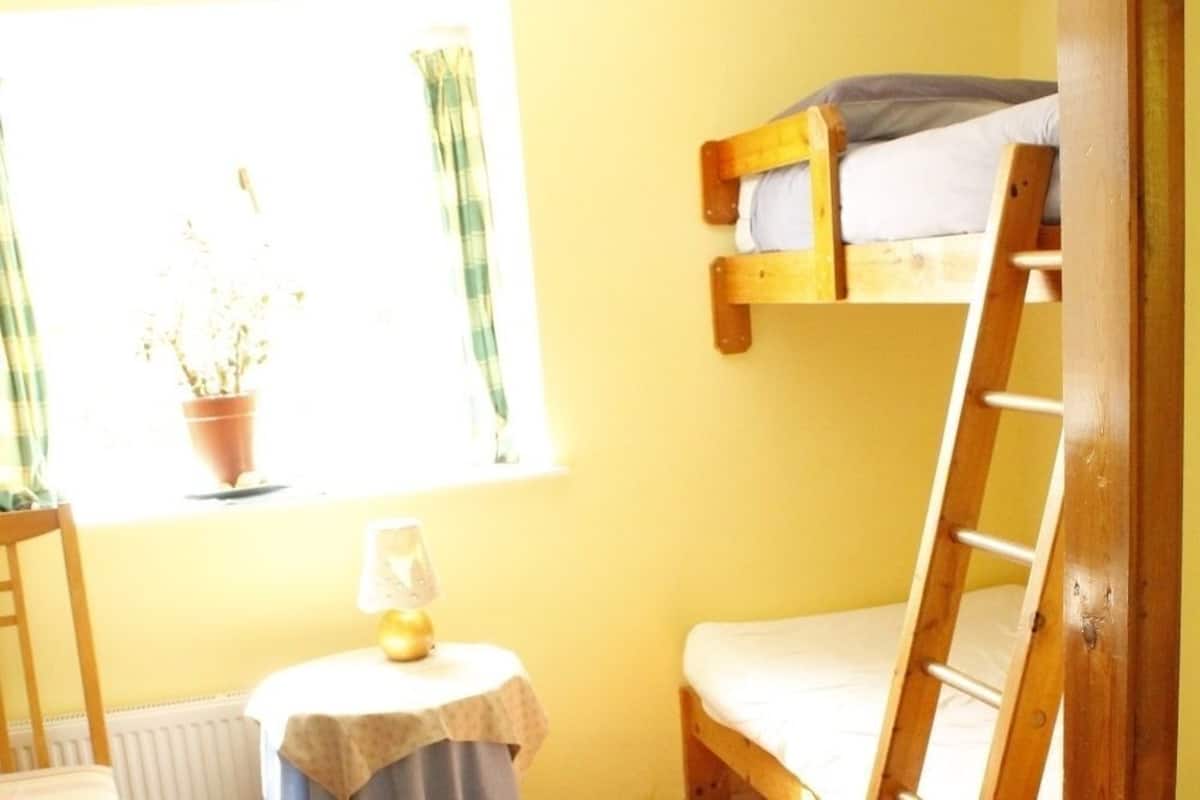 A bunk bed room with a window, a small table with a lamp, and a chair.