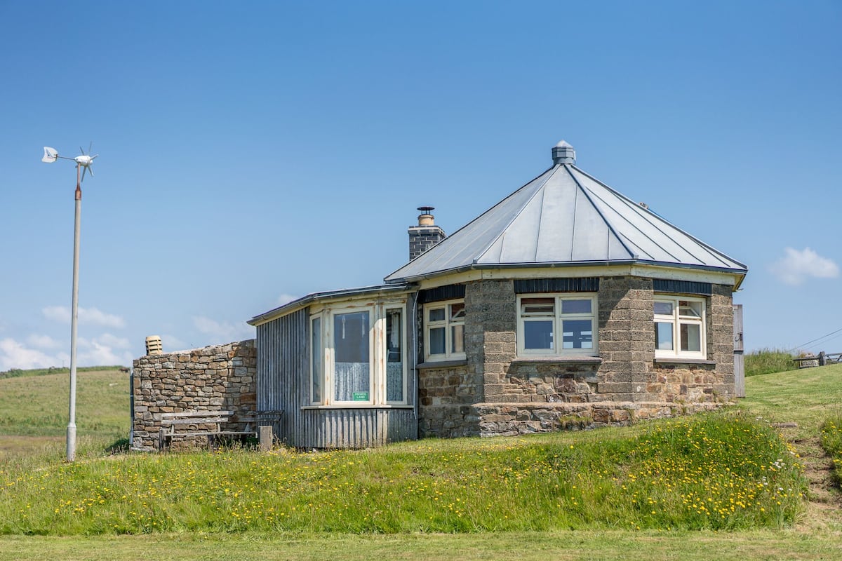 A stone house with a conical roof, a chimney, and a small porch.